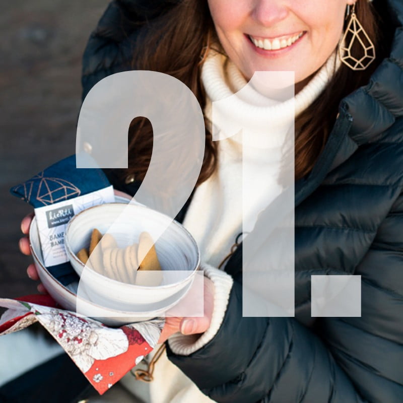 Numero 21, hymyilevä nainen pitää kädessä kulhoa, jossa pipareita, sekä tiskirätti ja kuviollinen lautasliina