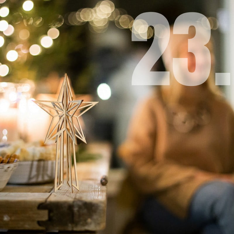 numero 23 puinen latvatähti pöydällä ja taustalla hymyilevä nainen ja joulukuusi